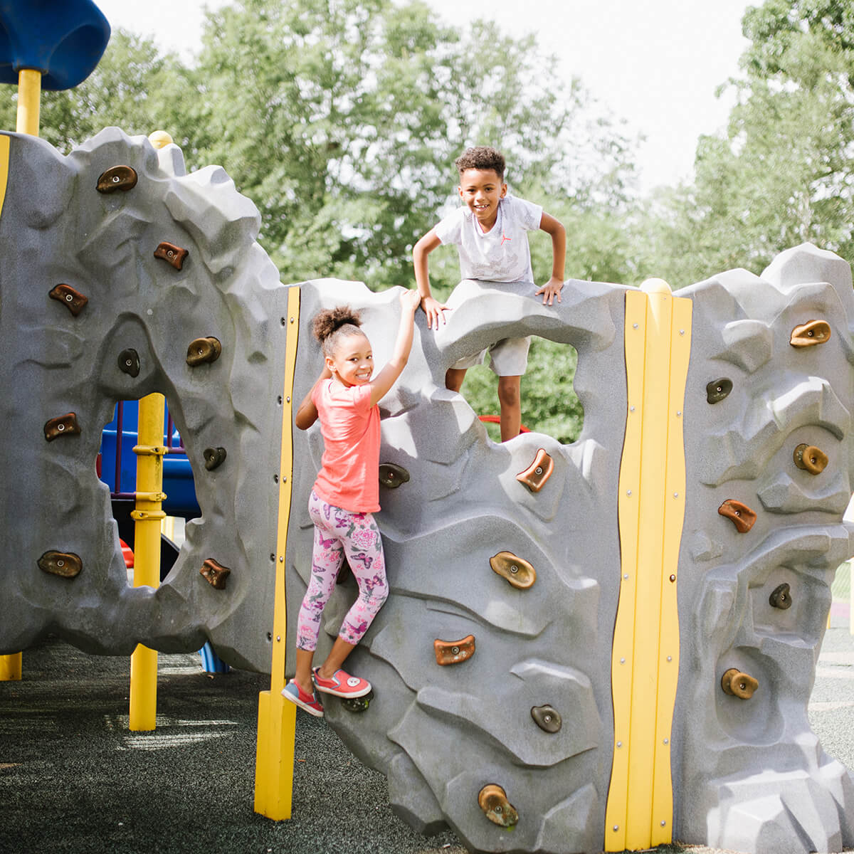 Two children climbing up and playing on a playground rock wall