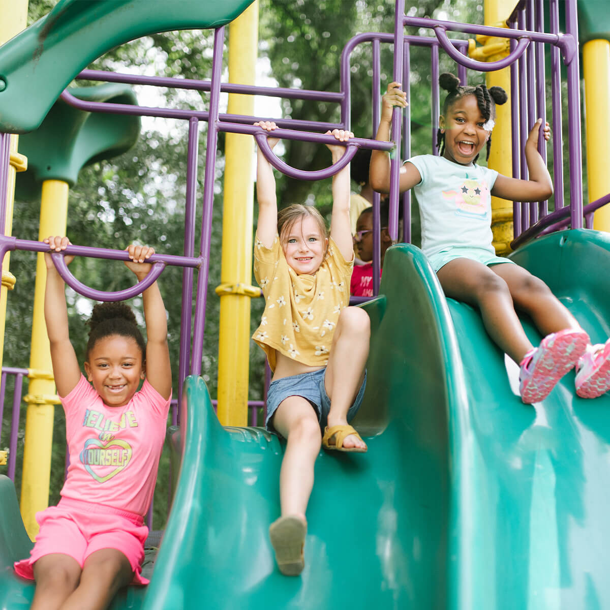 Three children sliding down a park's playground slide set